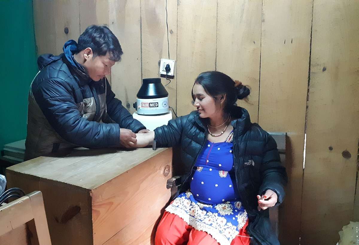 A lab assistant takes a blood sample from a pregnant woman at a rural health post