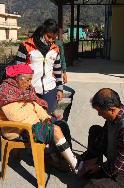 A technician fitting a leg brace for an elderly woman as a FAIRMED staff member watches